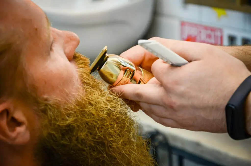 Do I Need to Trim my Beard? 
A barbers hands trimming a man's ginger mustache with gold trimmers.  
